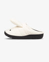 An off-white quilted slip-on mule shoe with a small black embroidered eye on the toe area and a thick black sole, shown against a plain light gray background.